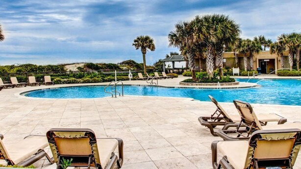 A pool area with lounge chairs, palm trees, and a building in the background. - Beautiful 2br/2ba Oceanfront, Sea Dunes  (Amelia Island)