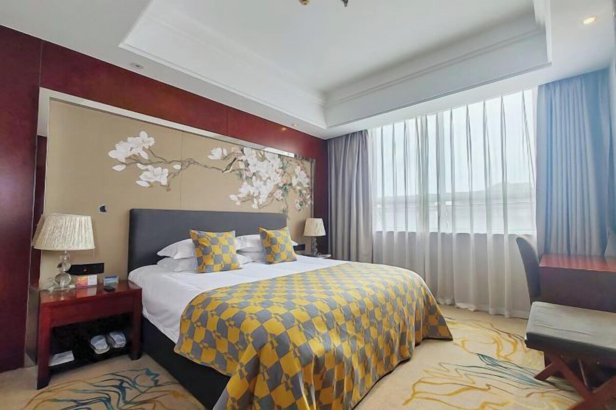 A hotel room with a large bed, a nightstand, a desk, and a chair.