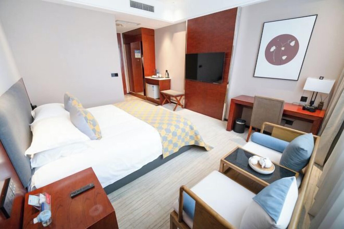 A hotel room with a bed, a desk, a chair, a TV, and a framed picture on the wall.
