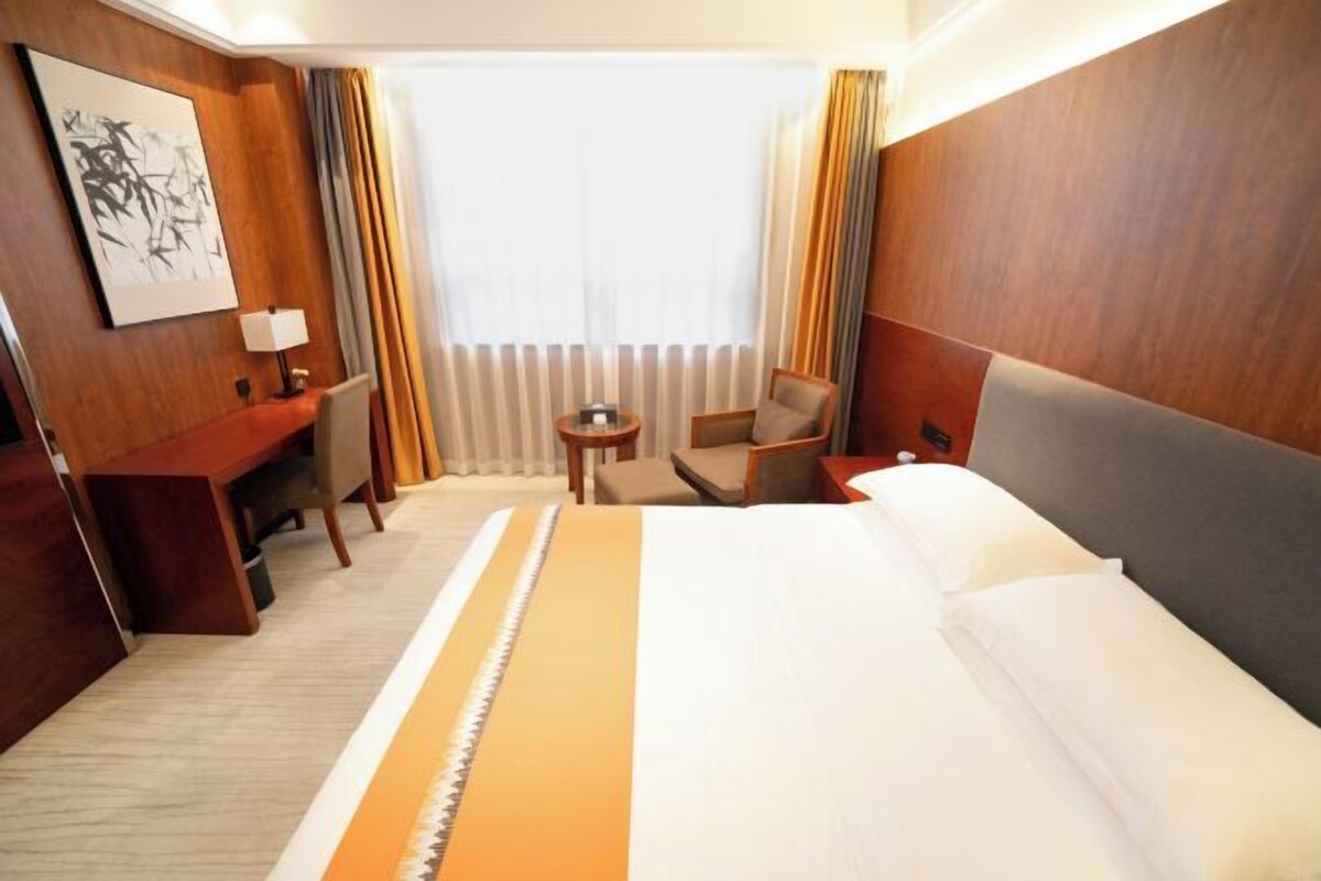 A hotel room with a large bed, a desk, a chair, and a small table.
