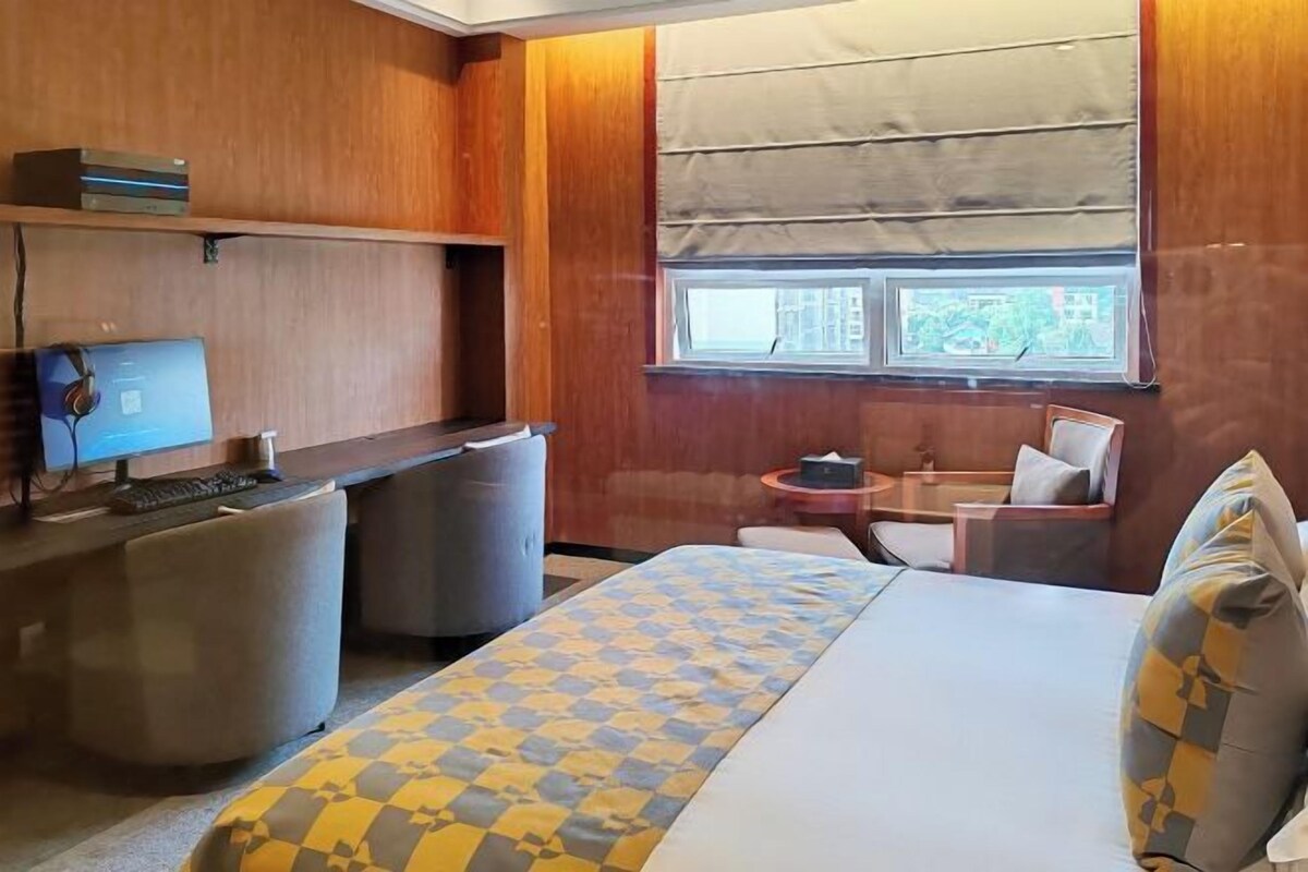 A hotel room with a bed, a desk with a computer, a chair, and a window with blinds.