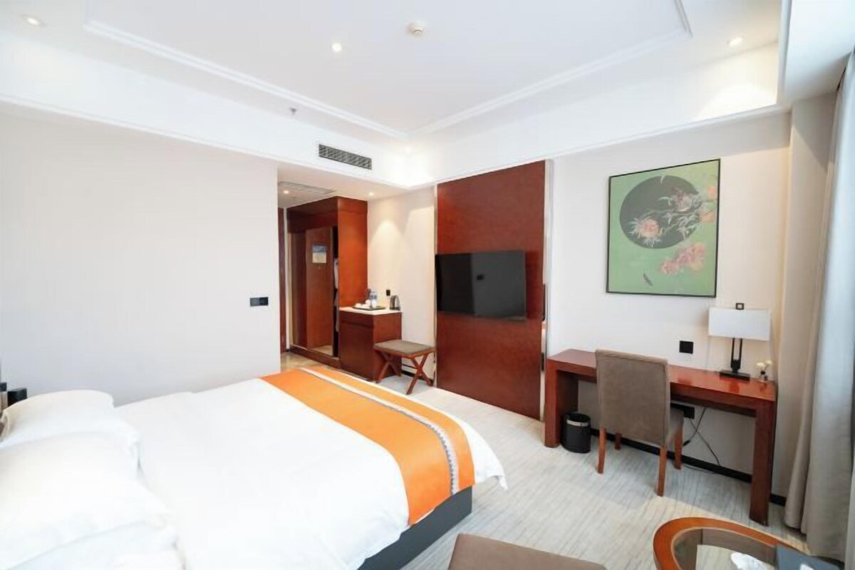 A hotel room with a bed, desk, chair, TV, and a painting on the wall.