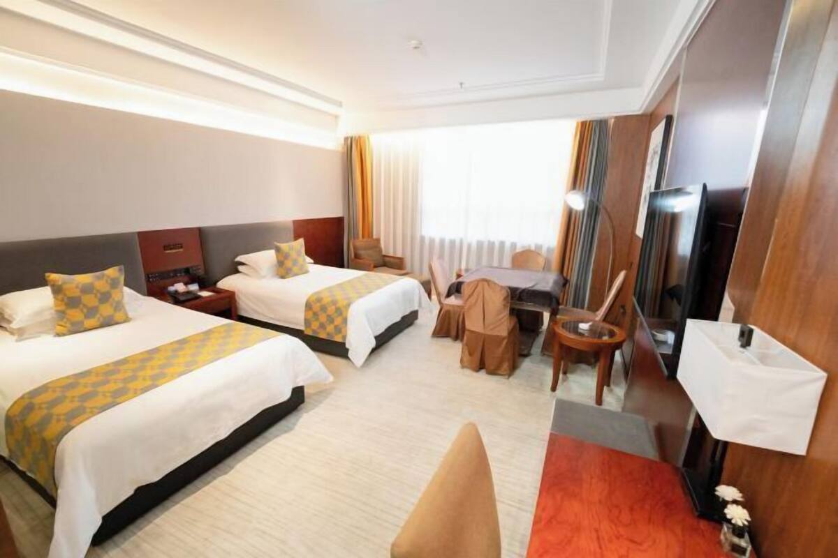 A hotel room with two beds, a desk, a chair, a TV, and a large window with curtains.