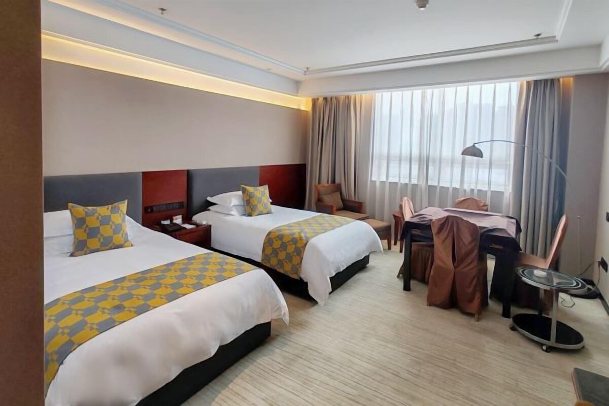 A hotel room with two beds, a desk, a chair, and a large window with curtains.