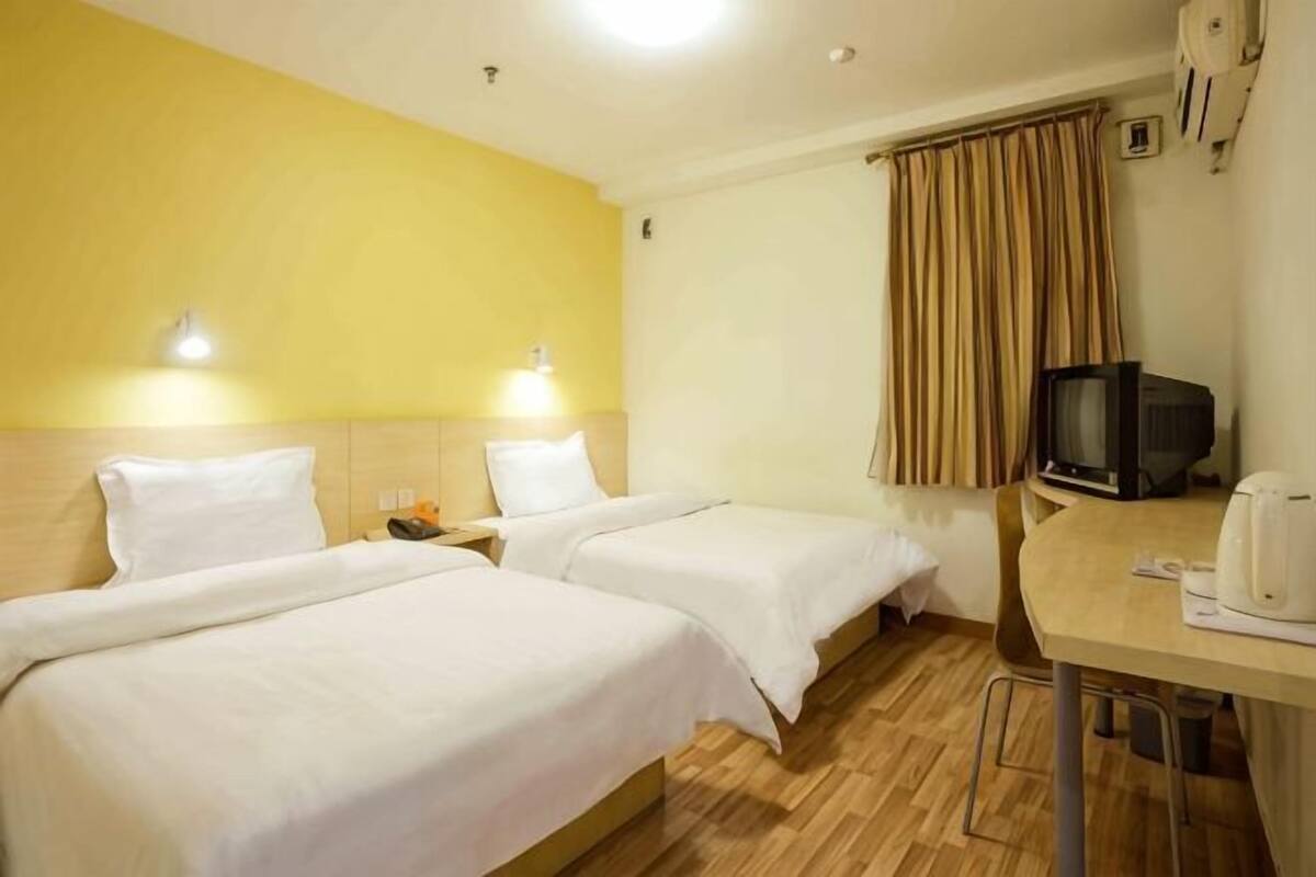A hotel room with two beds, a desk with a television, and a coffee maker.