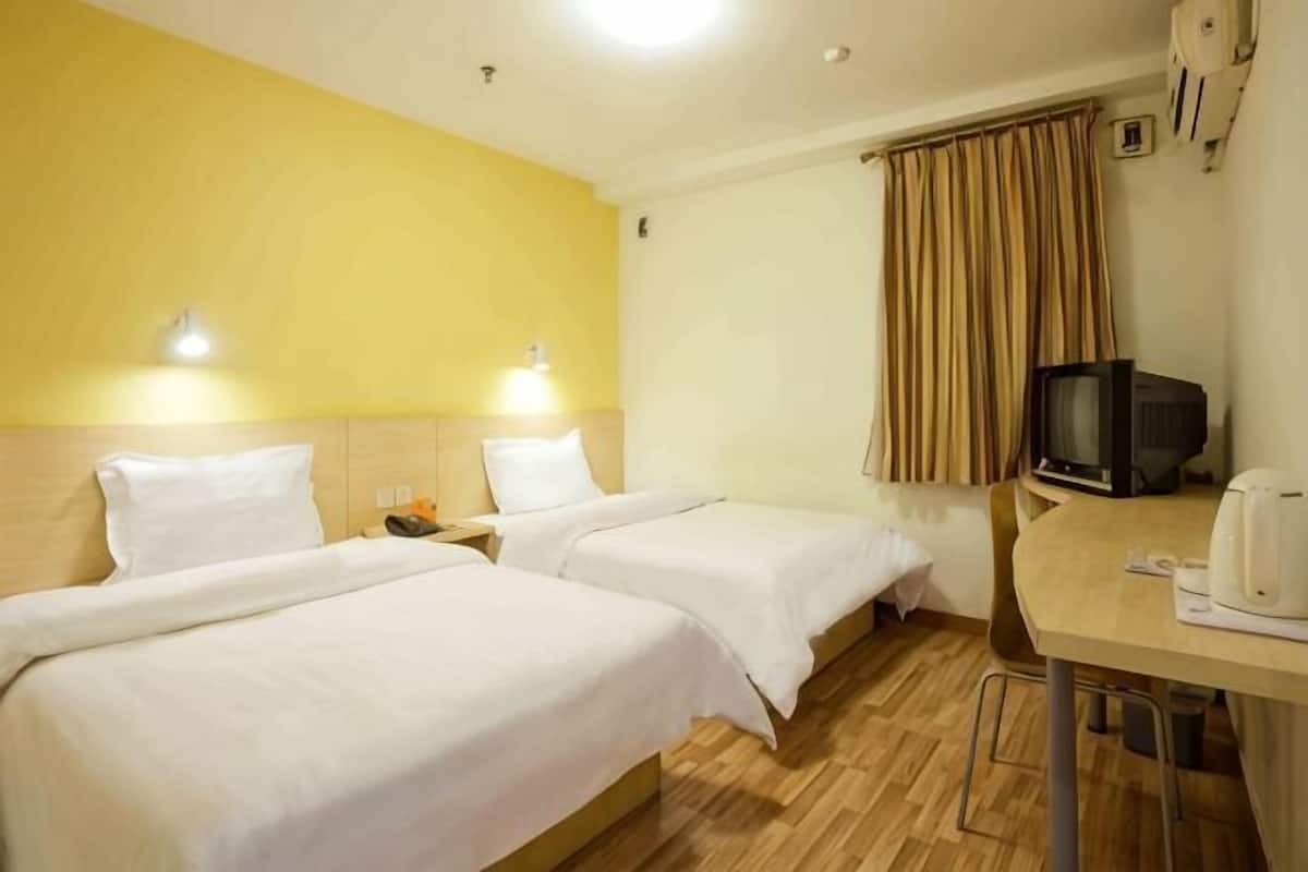 Una habitación de hotel con dos camas, un escritorio con televisor y una cafetera.