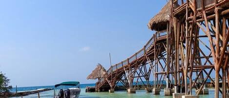 Una pareja en kayak en un mar tropical transparente, con bungalows sobre el agua al fondo.