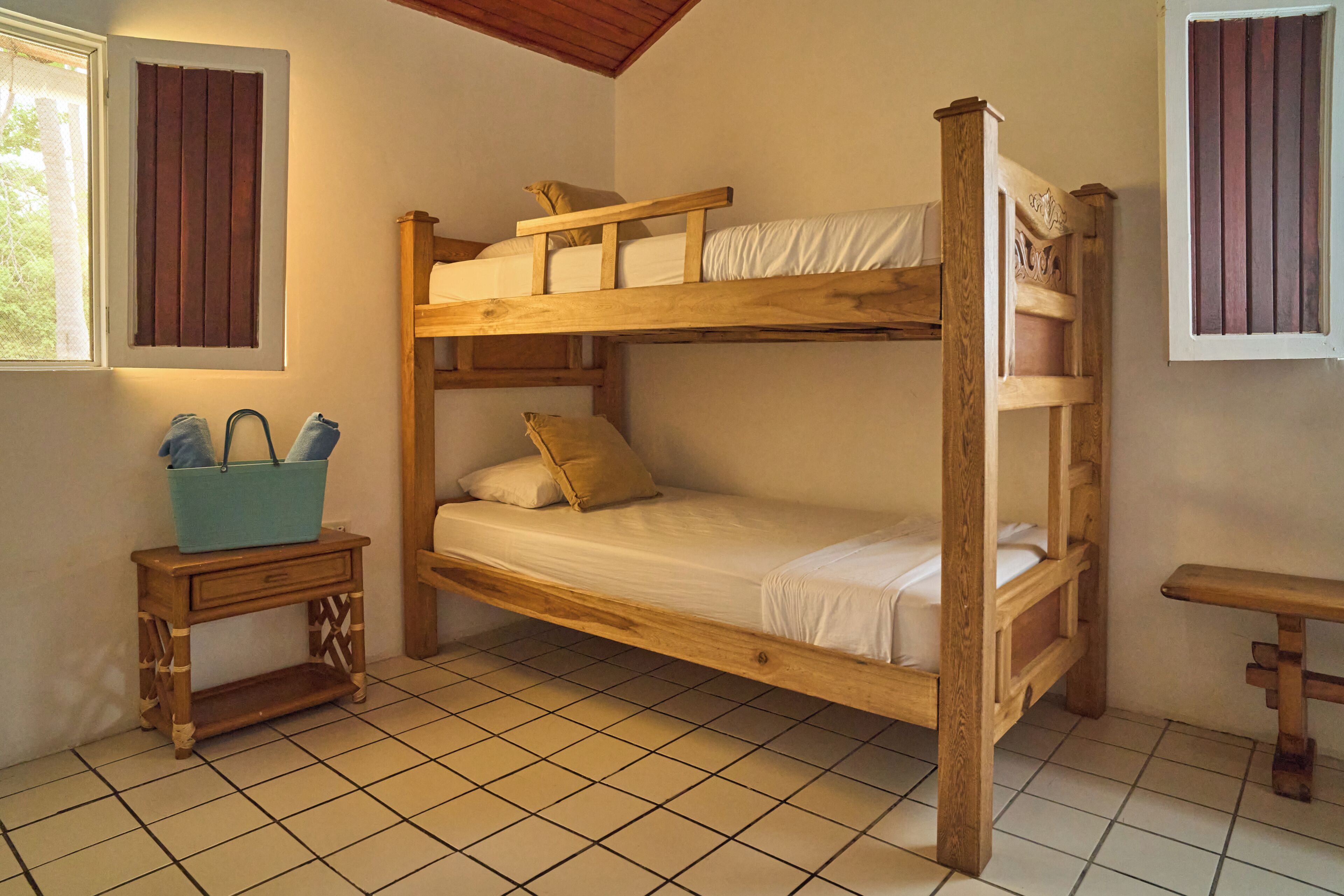 Dormitorio con literas, un banco de madera y una mesita con una cesta.