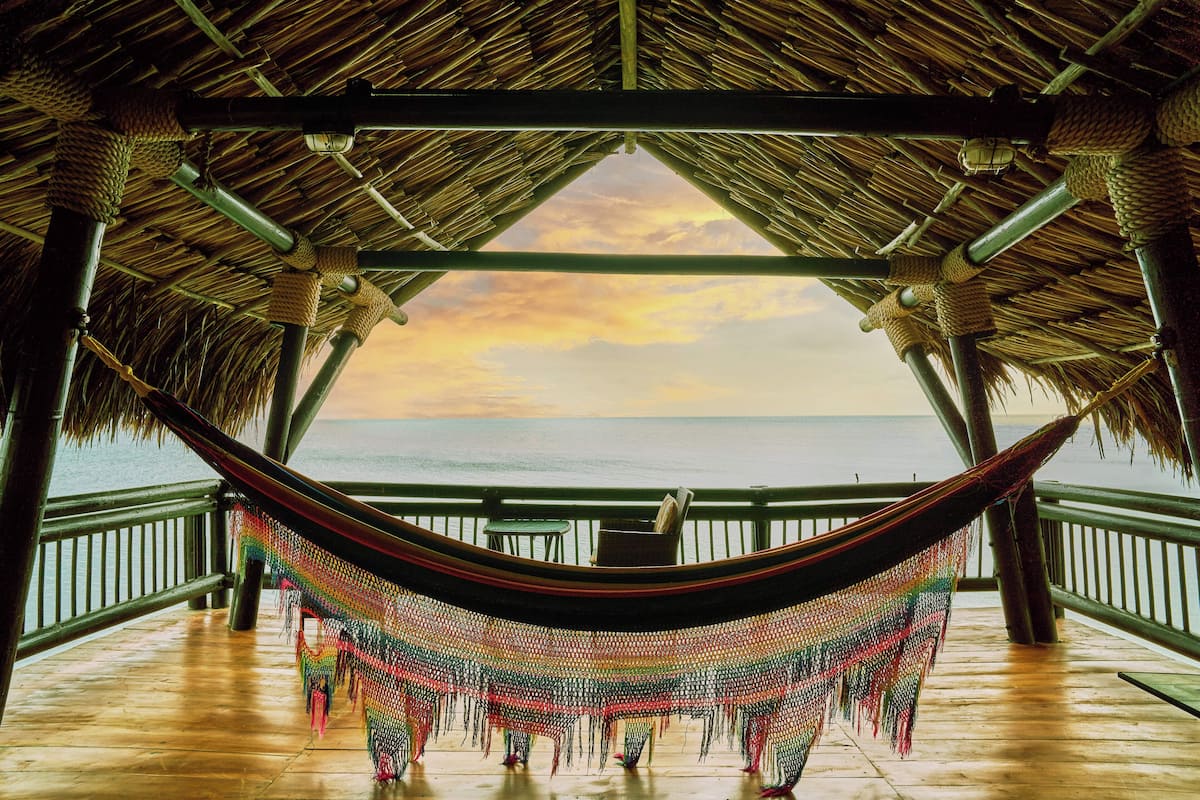 A hammock under a thatched roof structure with a view of the ocean.