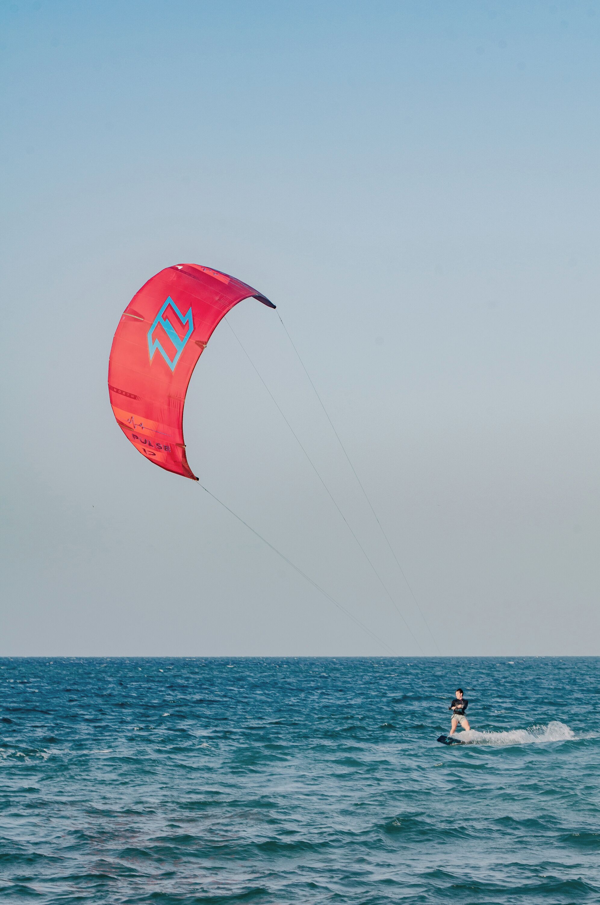 Una persona practicando kiteboarding sobre el agua, volando una cometa roja.