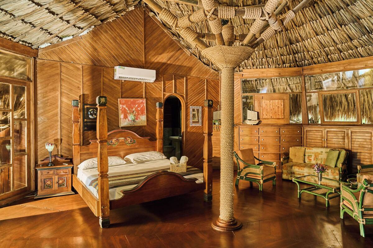 A room with a four-poster bed, wooden furniture, and a thatched roof.