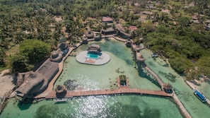 An aerial view of a resort with a central pool, thatched-roof structures, and a wooden bridge. - Mucura Club Hotel (Isla Mucura)