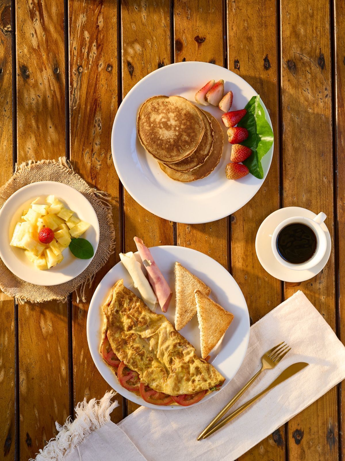 Uma mesa de madeira com panquecas, morangos, presunto, torradas e uma xícara de café para o café da manhã.
