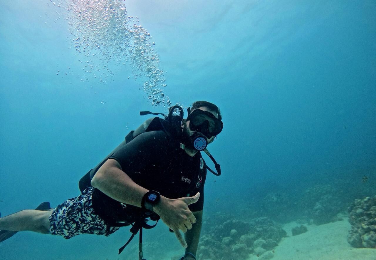A diver underwater with a scuba mask and fins, surrounded by bubbles and a rocky seabed.