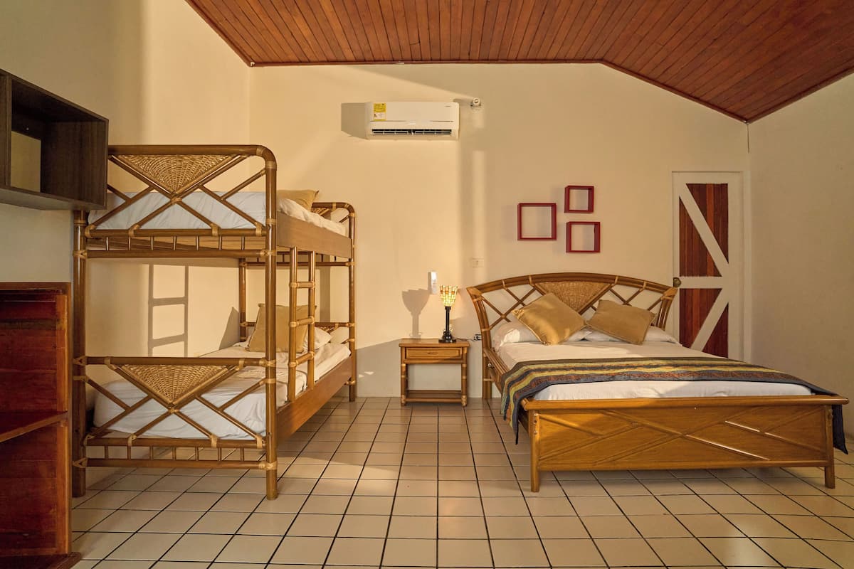 A room with a bunk bed, a single bed, a nightstand with a lamp, an air conditioning unit, and a door with a striped pattern.