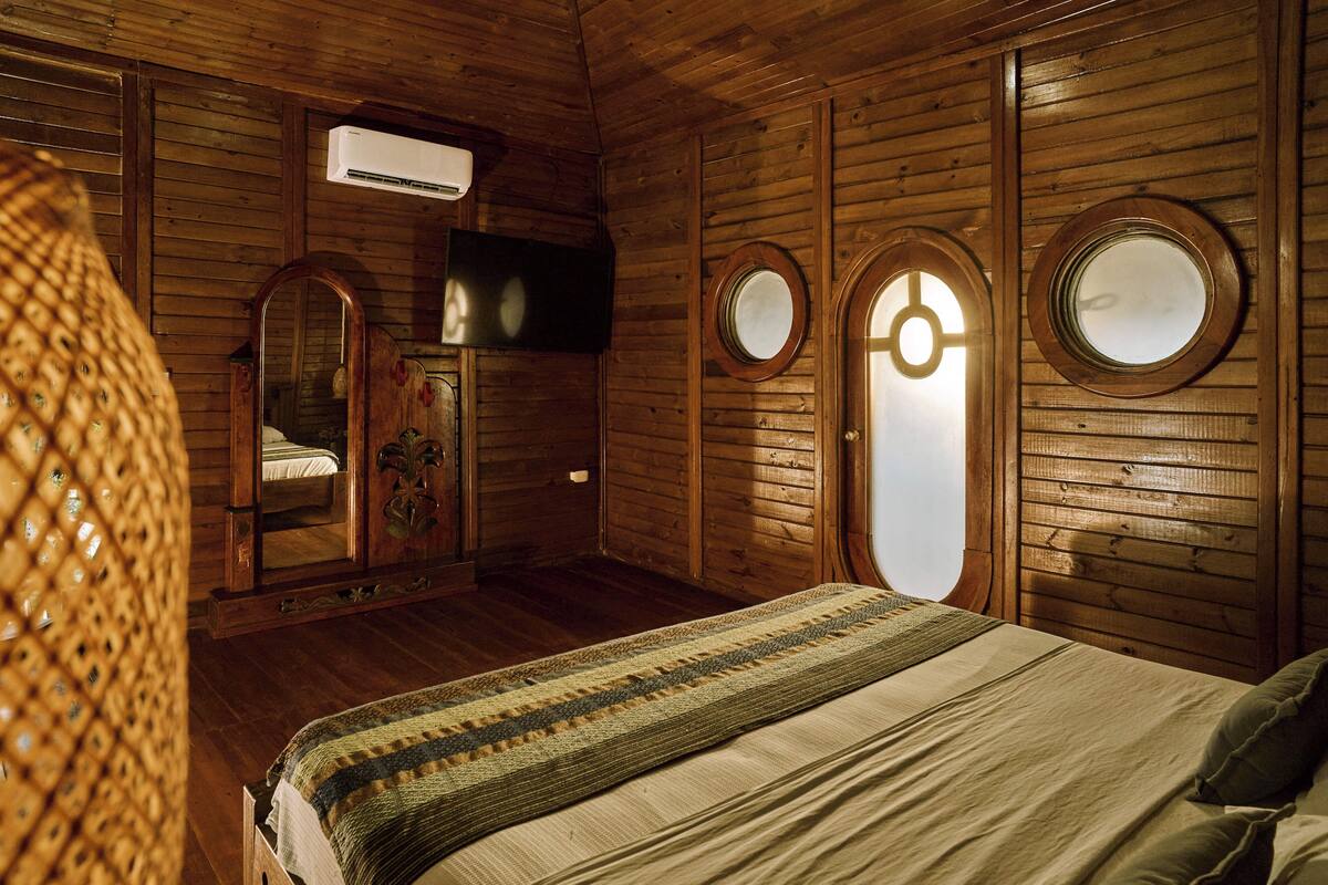 A wooden room with a bed, a mirror, and a television.