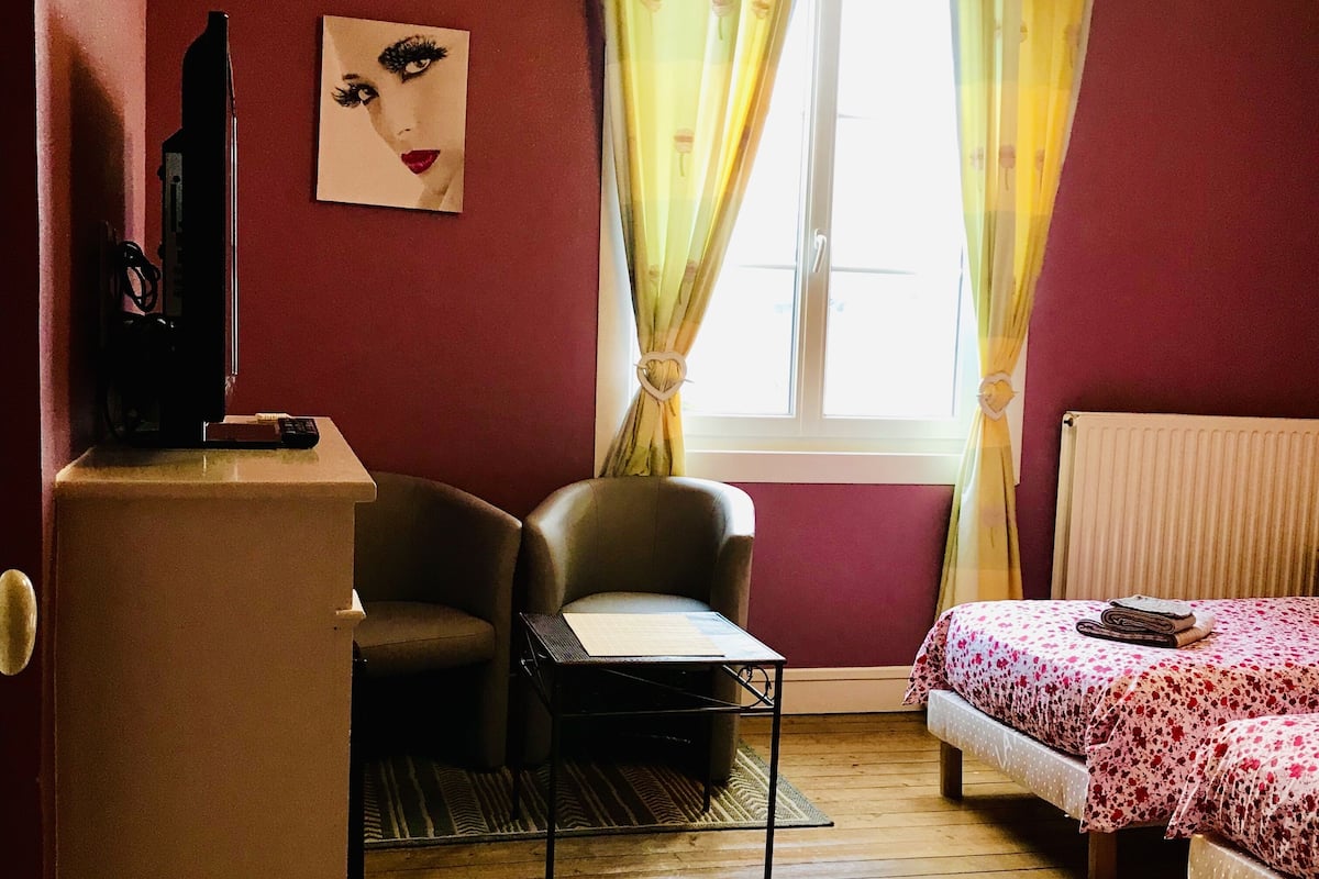 A small, cozy room with a single bed, a chair, a desk, and a television.