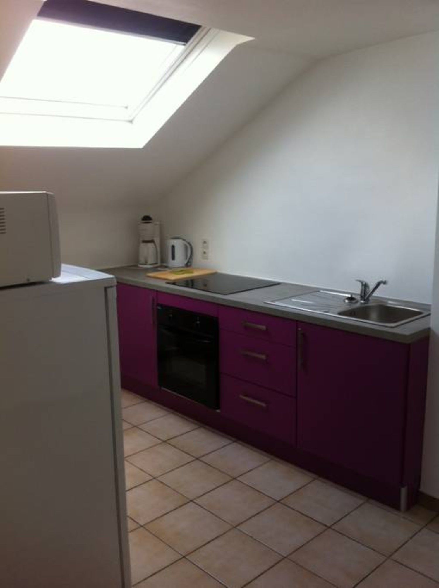 A compact kitchen with a built-in oven, a sink, and a window above the countertop.