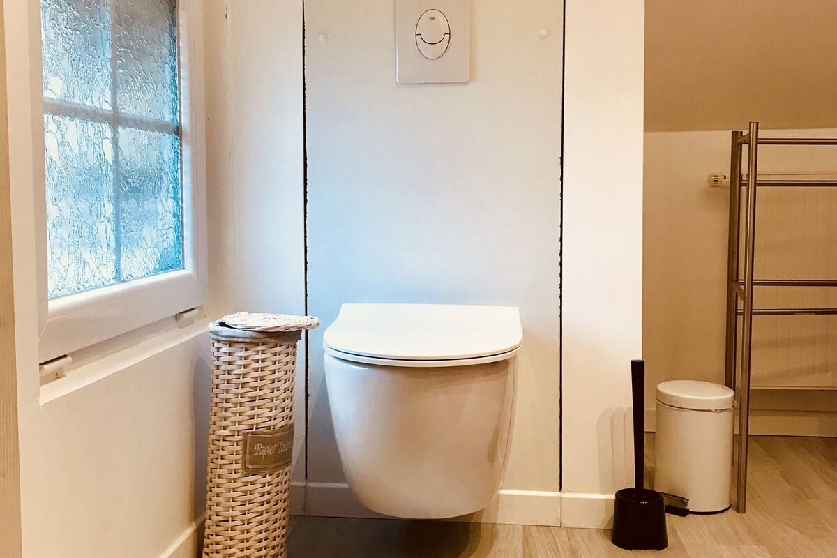 A bathroom with a toilet, a wicker trash bin, a window, and a metal towel rack.