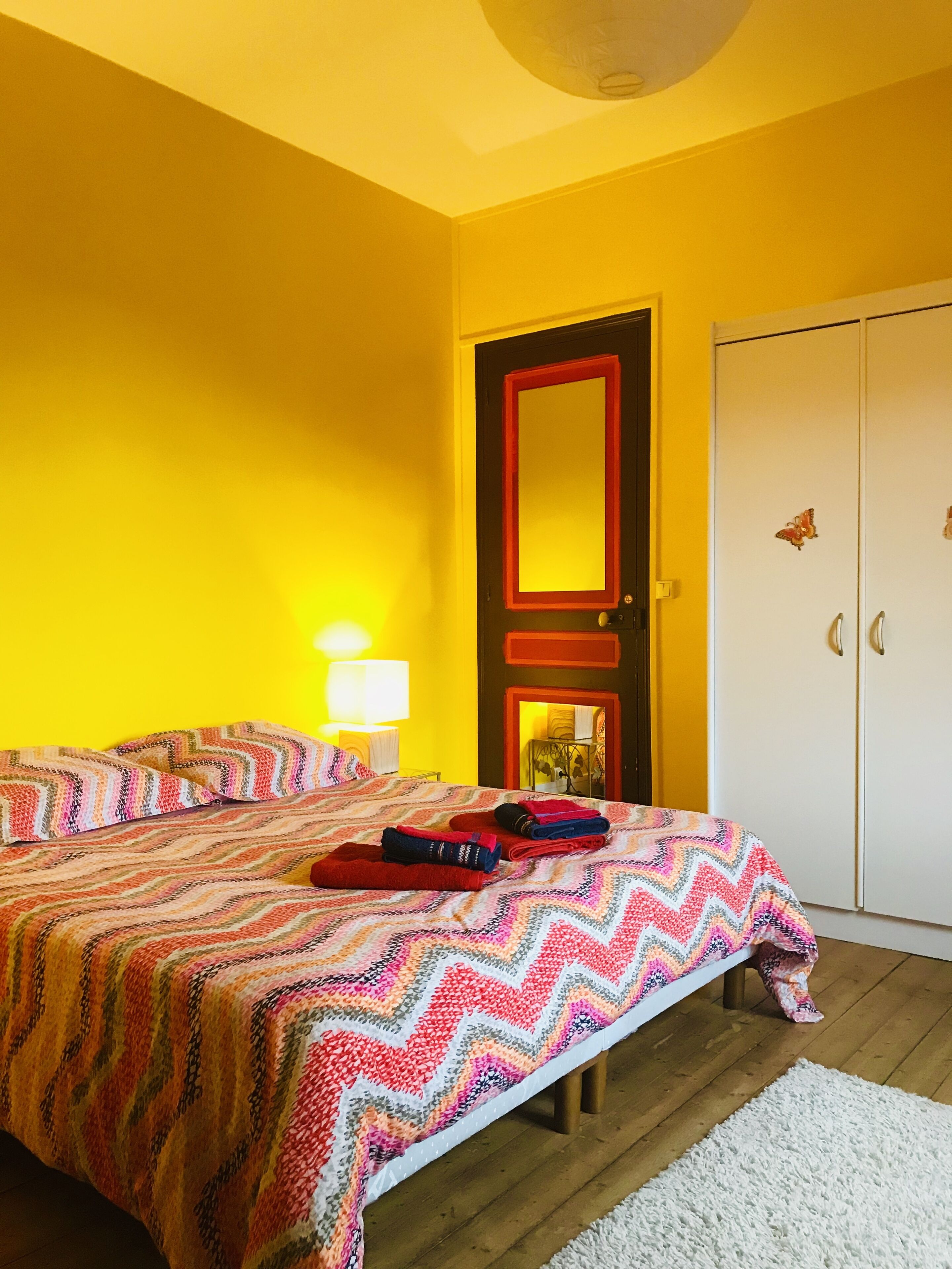 A bedroom with a bed, a wardrobe, and a mirror.