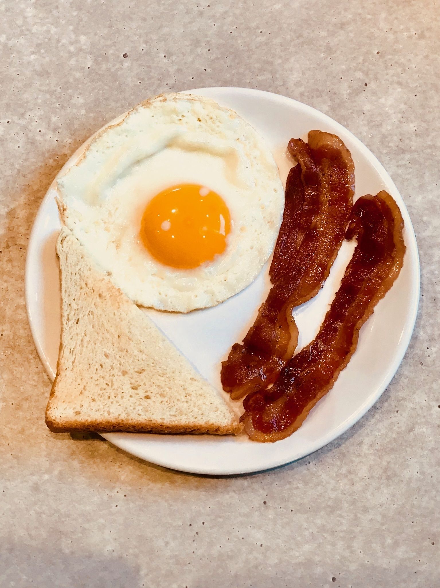 A plate with a fried egg, bacon, and a slice of toast.