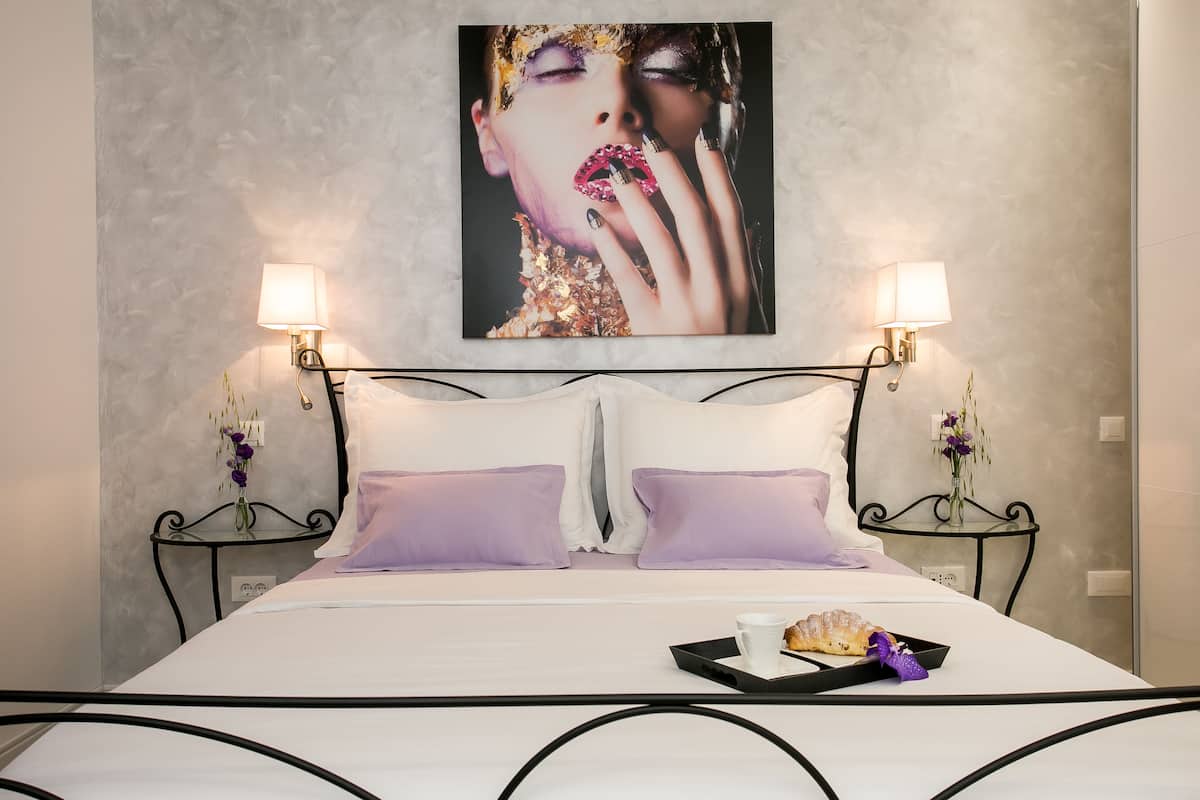 A neatly made bed with two pillows, a tray with a croissant and a cup, and two wall-mounted lamps.