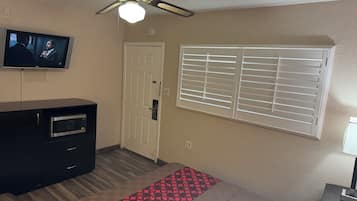 Une chambre d’hôtel équipée d’un lit, d’une télévision, d’un ventilateur de plafond, d’une fenêtre avec des stores et d’une porte.