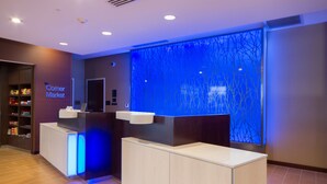 A reception area with a blue-lit wall, a counter, and a shelf with toiletries. - Fairfield Inn & Suites by Marriott Buffalo Amherst/University (Buffalo)