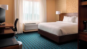 A hotel room with a bed, a desk, a chair, a TV, a window with curtains, and an air conditioning unit.