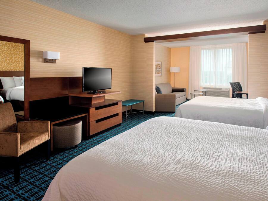 A hotel room with two beds, a TV, a desk, a chair, and a window with curtains.
