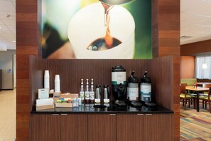 A hotel reception area with a coffee station, a large abstract painting, and a seating area in the background. - Fairfield Inn & Suites by Marriott Buffalo Amherst/University (Buffalo)