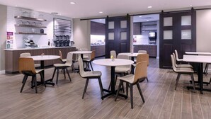 Un restaurante moderno con mesas y sillas redondas, una zona de cocina y vistas por un toldo corredero.