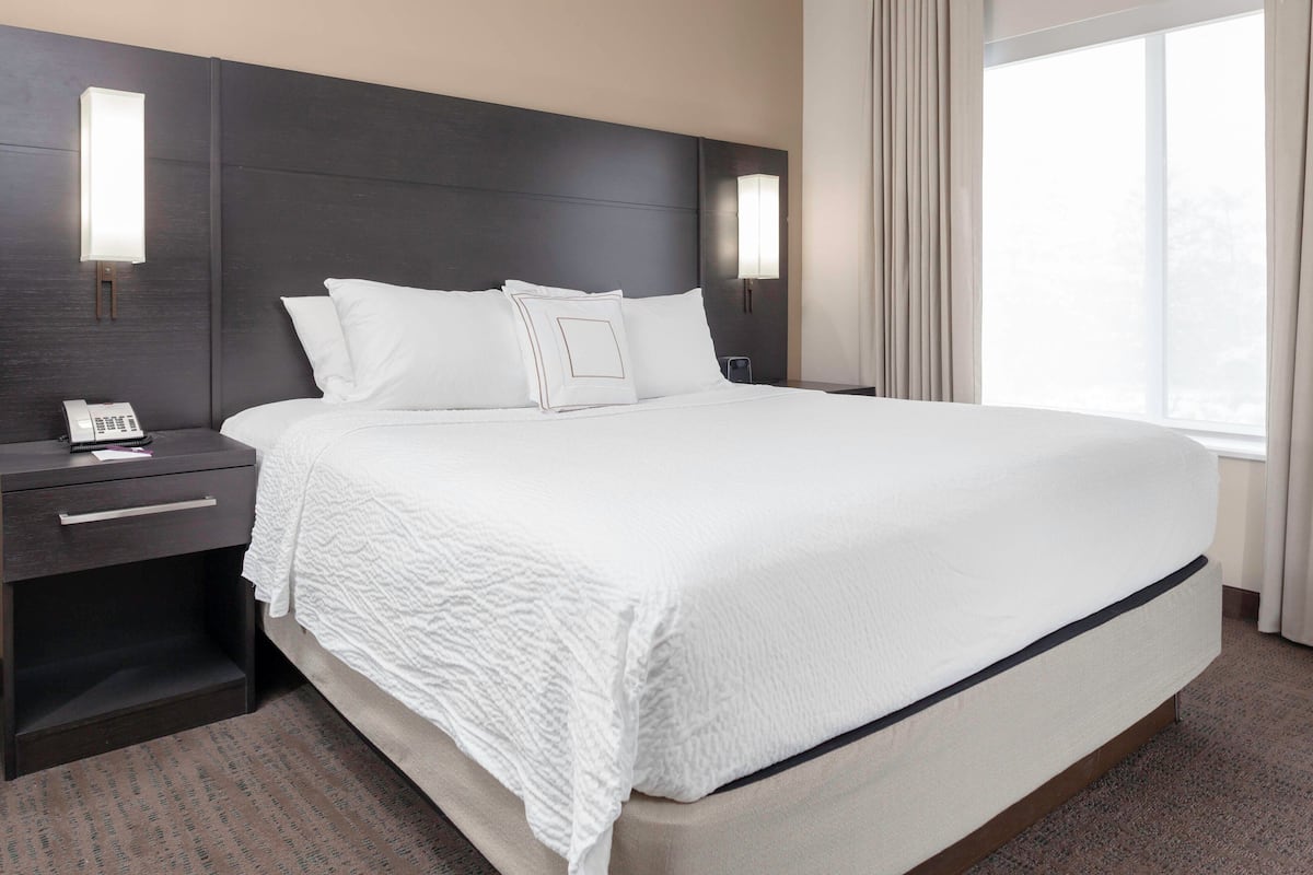 A hotel room with a large bed, dark headboard, bedside tables, and a window with curtains.