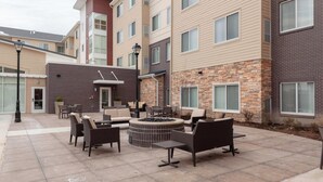 Un patio con mobiliario exterior, una fogata y un edificio de ladrillo con varias ventanas.