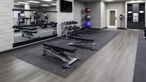 Un gimnasio con equipo de ejercicio, un espejo y un televisor instalado en la pared.