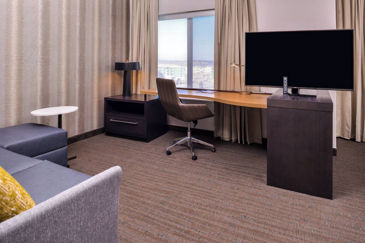 Habitación de hotel con una televisión de pantalla plana grande, un escritorio con una silla, un sofá y una mesita.
