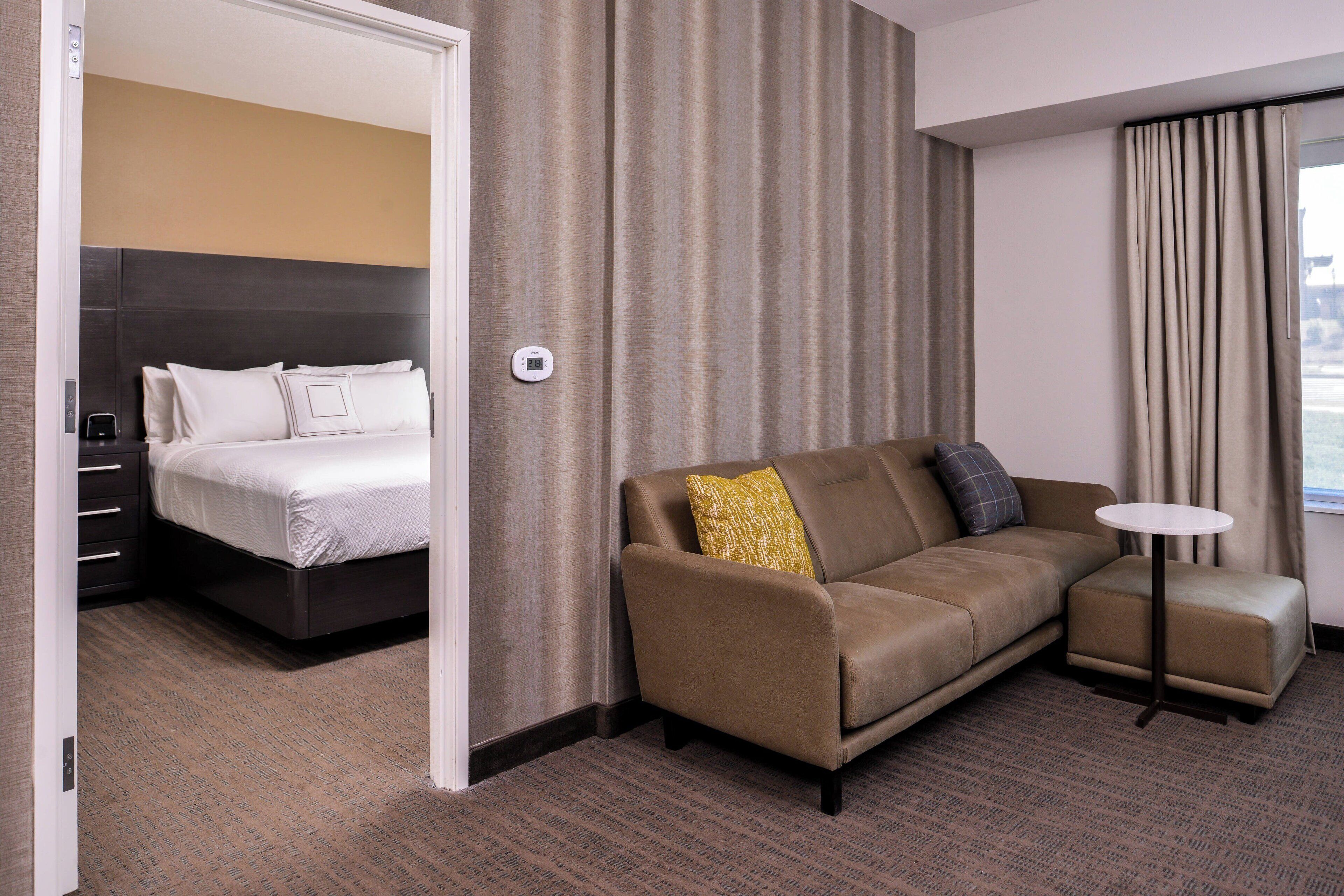 A hotel room with a bed, a sofa, a small table, and a window with curtains.