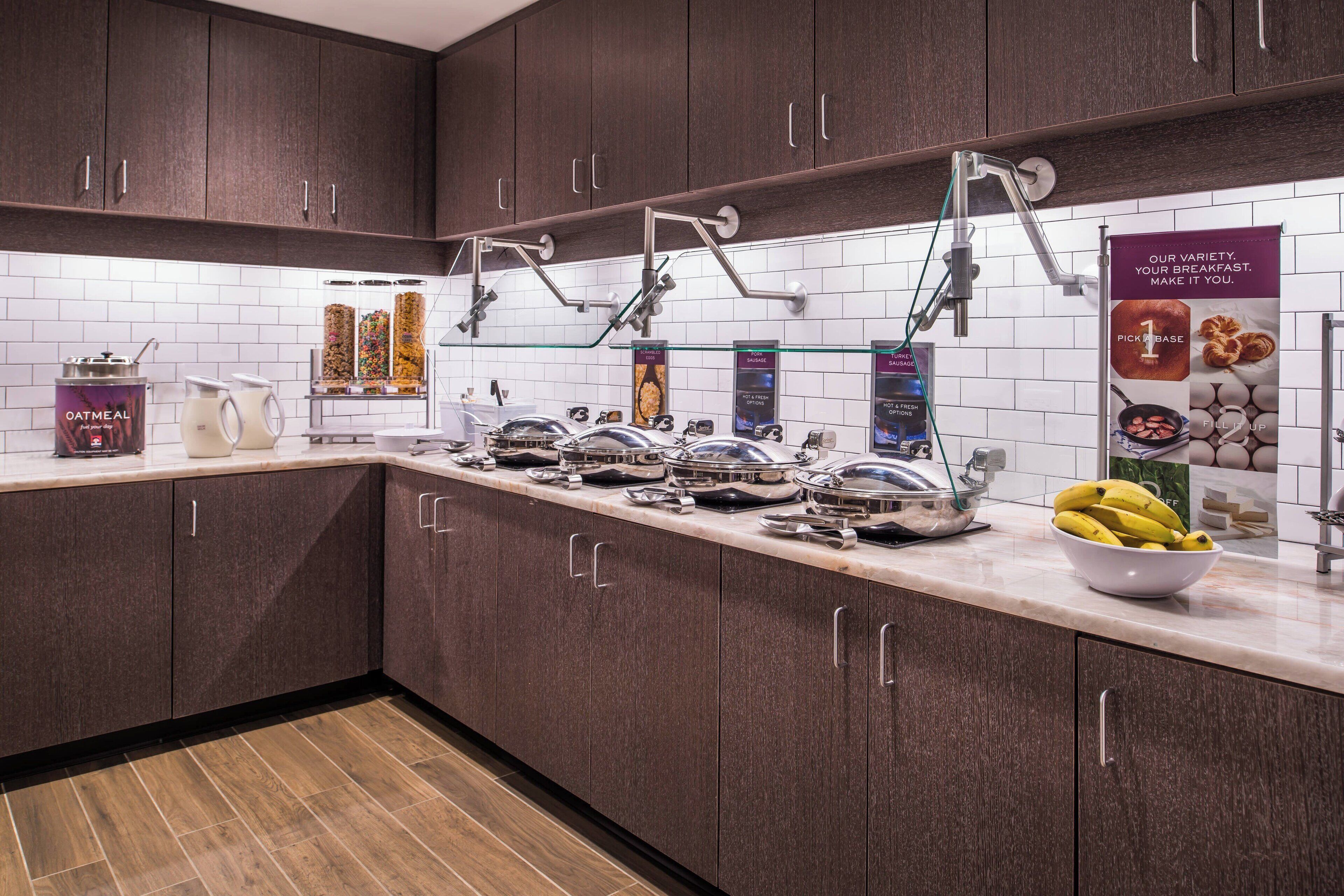 A modern kitchen with dark wooden cabinets, a white tiled backsplash, and a variety of breakfast items on the counter.