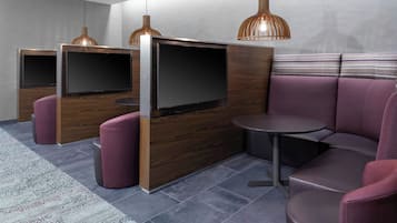 Ein modernes Zimmer mit einer Holzwand, einem Flachbildfernseher und einer Sitzecke mit rundem Tisch und gepolsterten Stühlen.