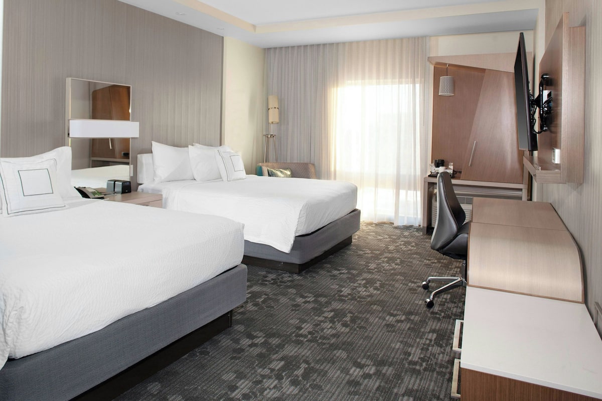 A hotel room with two beds, a desk, a chair, a TV, and a wardrobe.