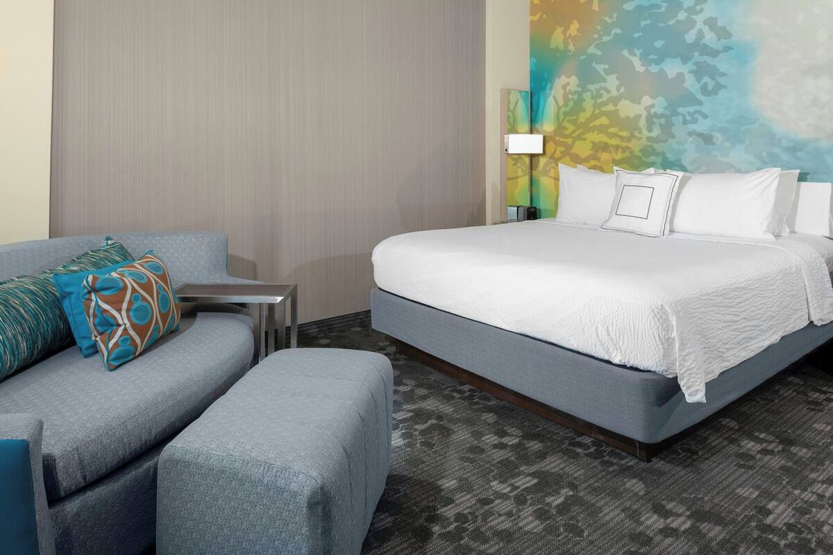A hotel room with a bed, a sofa, a small table, and a lamp.