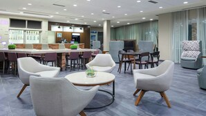 Un hall d’hôtel moderne doté d’un bar, de différents espaces de détente et offrant une vue sur le paysage urbain grâce à de grandes fenêtres.