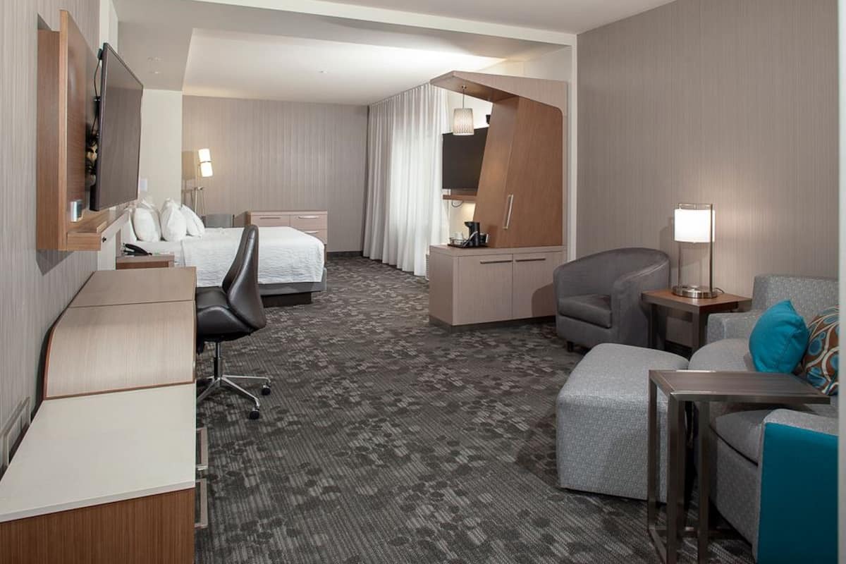 A hotel room with a bed, a desk, a chair, a sofa, and a TV.