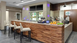 Un espace bar moderne avec un comptoir en bois, des tabourets de bar et une présentation de fruits et de boissons.