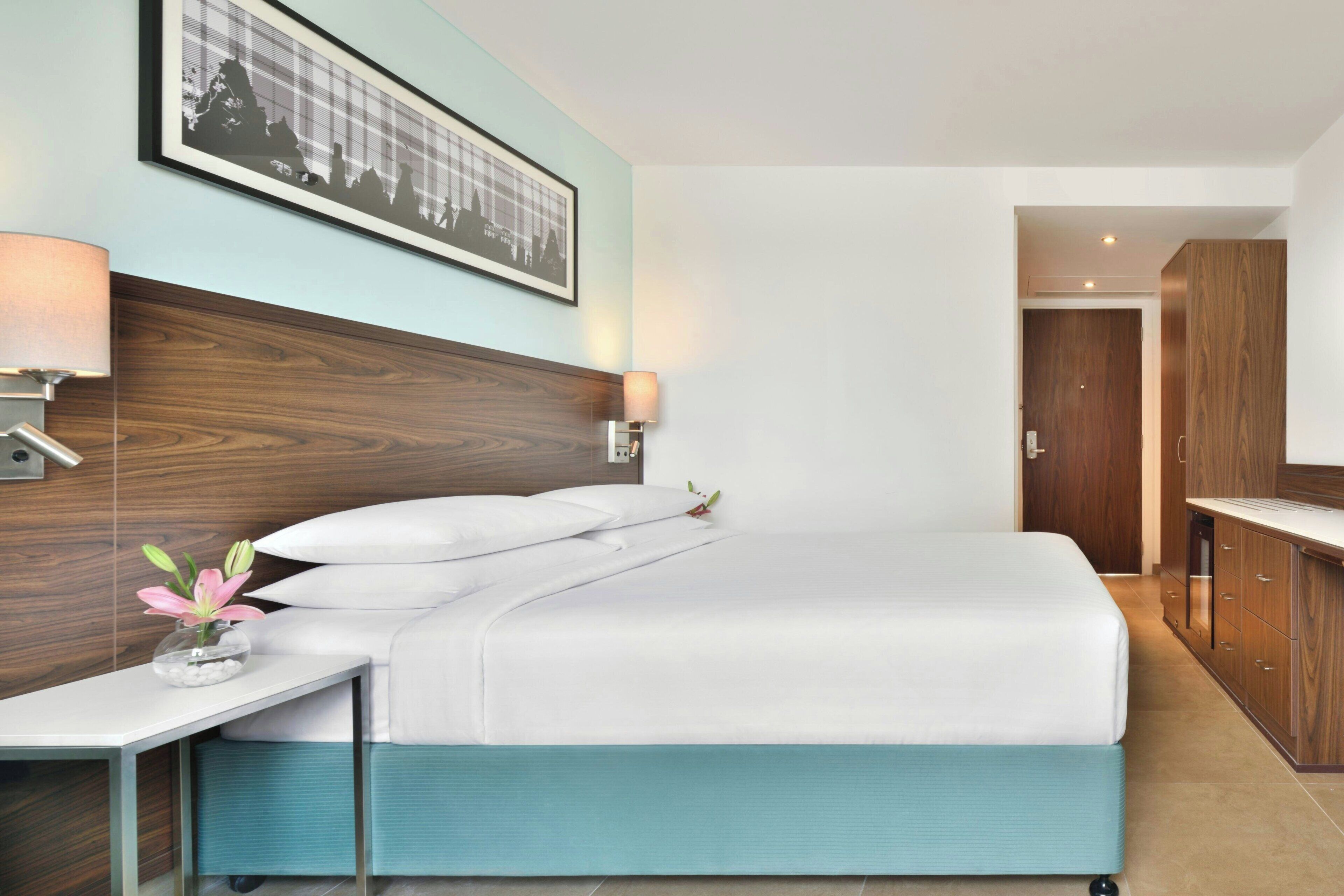 Camera d'albergo con un letto, comodini, una lampada a parete, un quadro incorniciato e un armadio in legno.