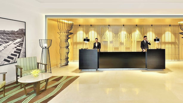 Eine moderne Hotellobby mit einer Rezeption, zwei Mitarbeitern, einem großen gerahmten Foto und einem gemusterten Teppich.