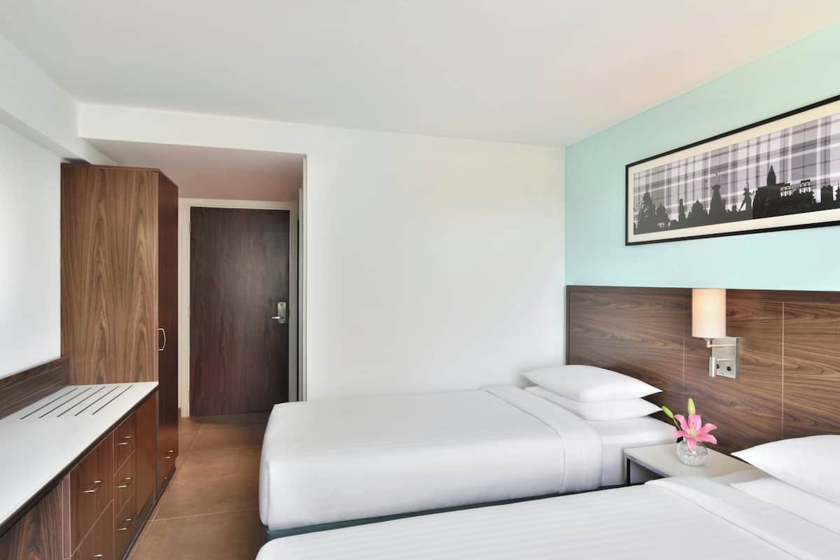 Een hotelkamer met twee bedden, een houten garderobe, een stadsbeeld in een lijst en een nachtkastje met een bloevas.