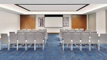 A conference room with rows of chairs, a large screen, and framed artwork on the walls.