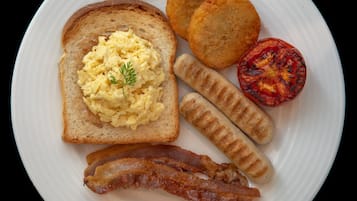 Ein Teller mit Rührei, Toast, Würstchen, gegrillter Tomate und Speck.