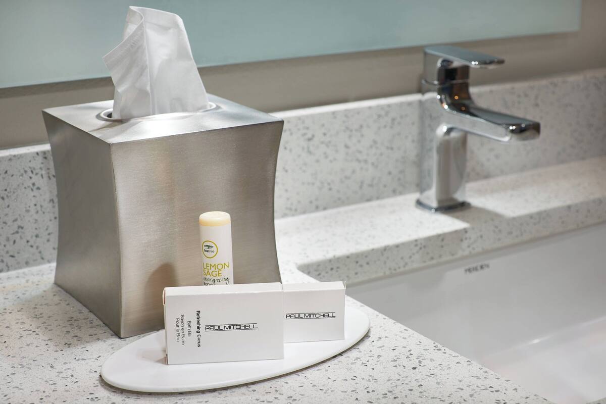 A bathroom with a tissue box, a bottle of Paul Mitchell Lemon Sage body spray, and a Paul Mitchell box on a countertop.